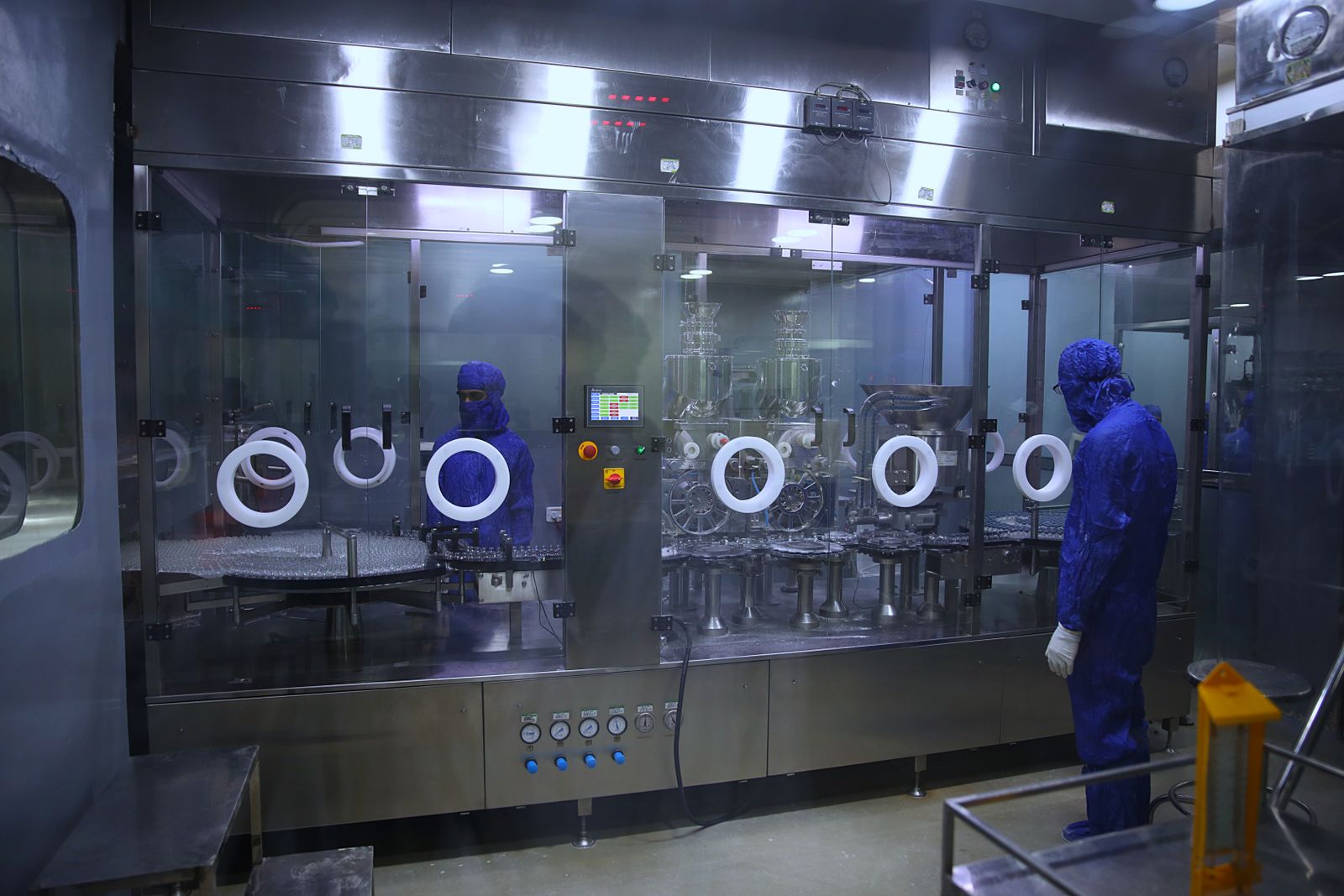 Technicians in cleanroom suits operating sterile pharmaceutical filling equipment